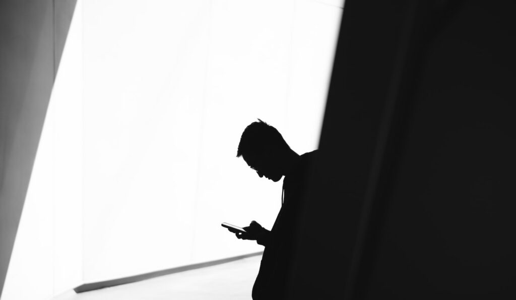 Qui sommes-nous ? 1 person using phone leaning on wall in silhouette photography